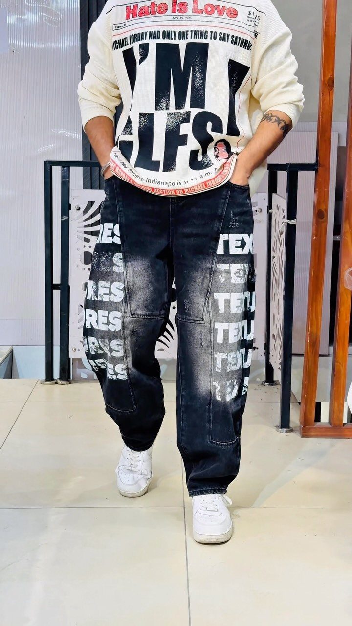 Person wearing a white graphic sweatshirt and baggy black patterned denim jeans with white sneakers.