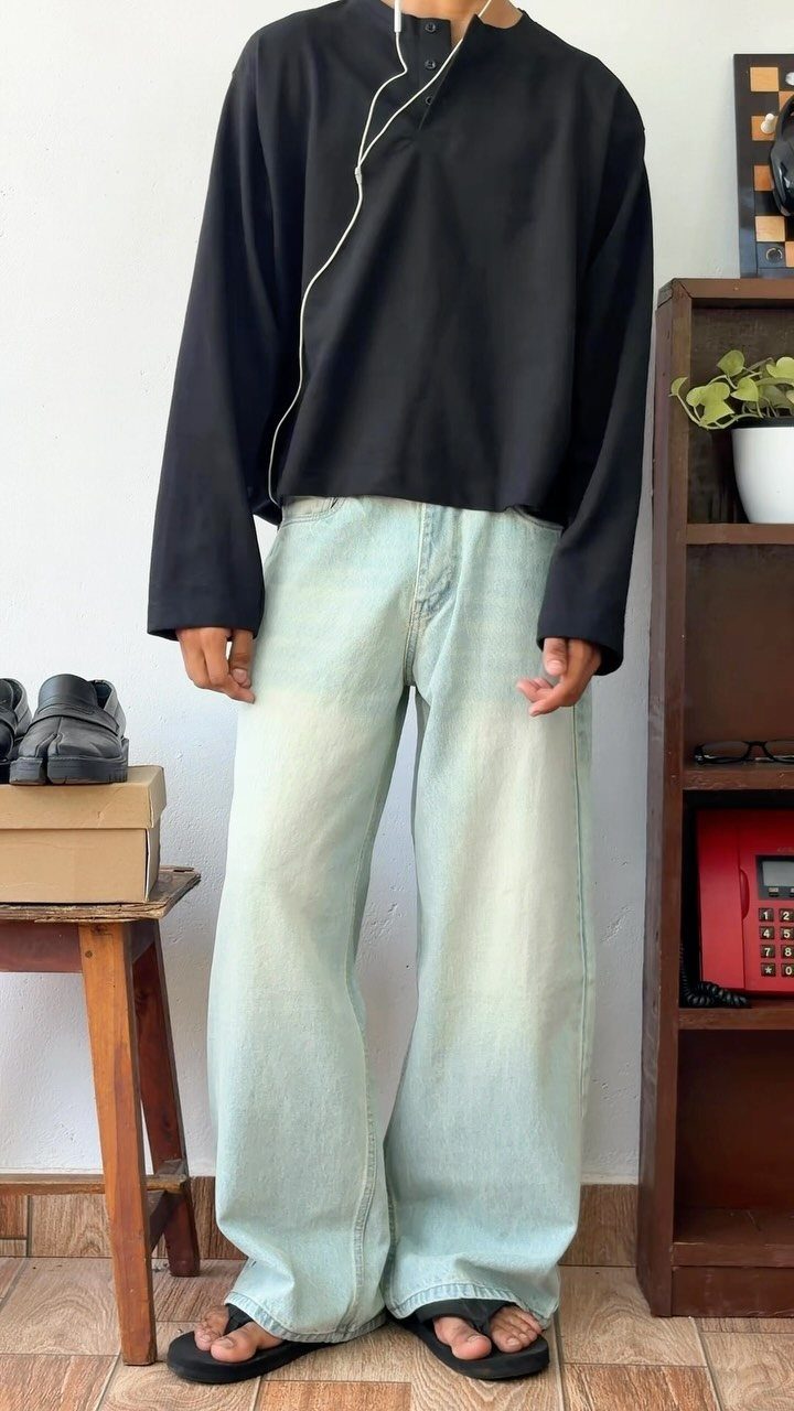 Person wearing an oversized black shirt and baggy light-wash denim jeans standing indoors.