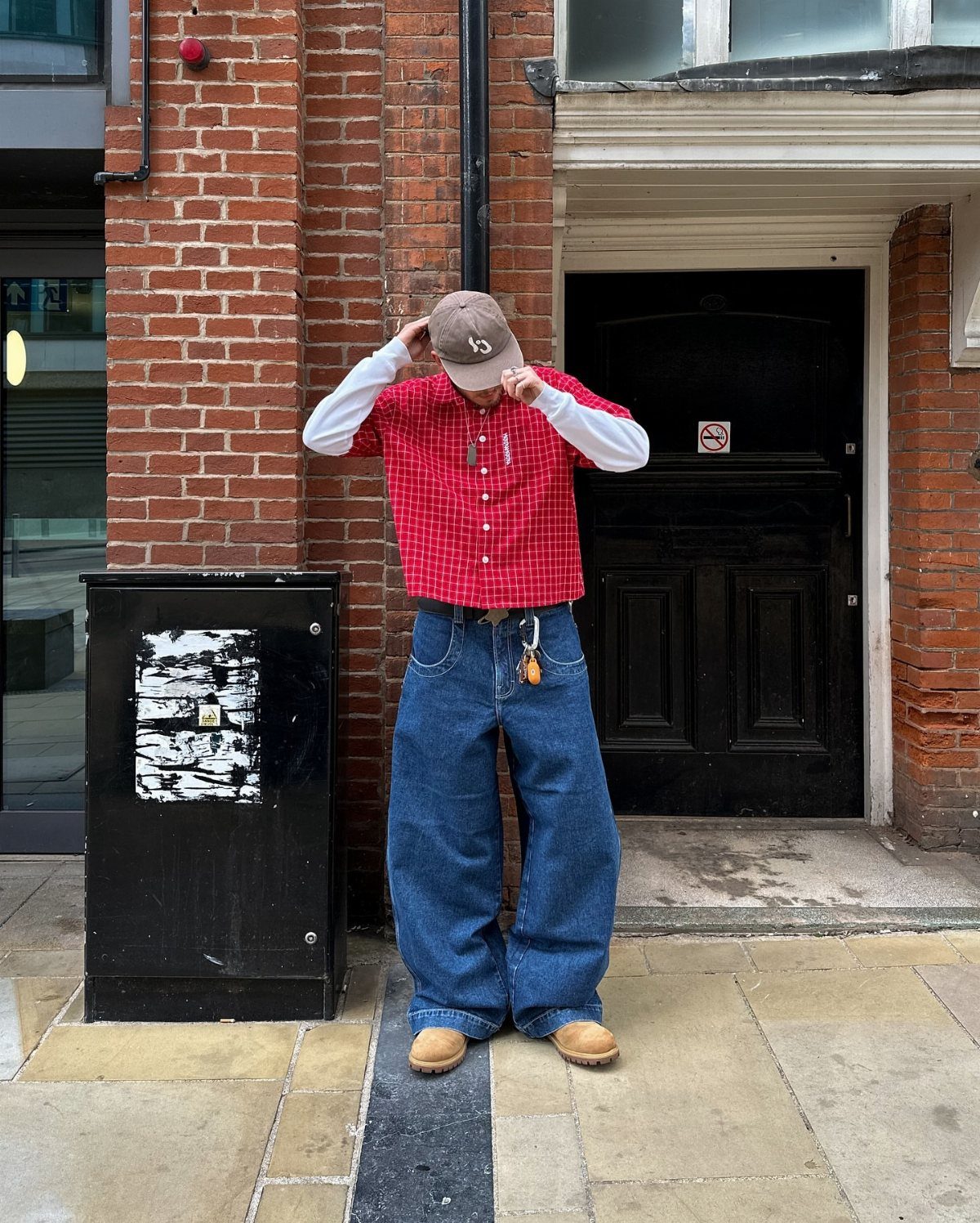 Man in red checkered shirt and baggy blue jeans wearing tan chunky boots.