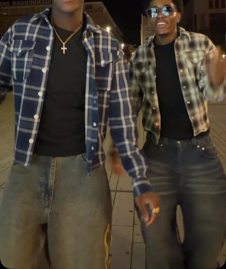 Two men walking at night wearing baggy jeans and plaid shirts.