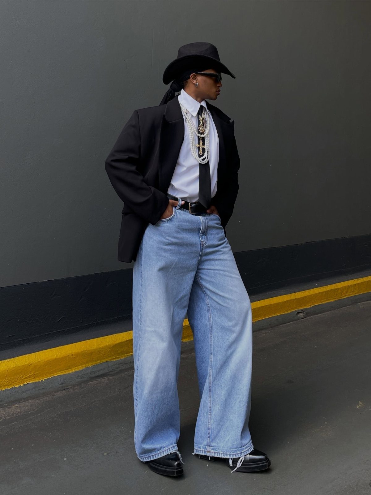 Person wearing baggy jeans, a black blazer, white shirt, and black cowboy hat.