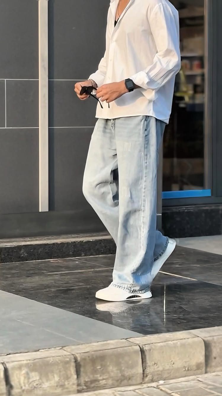 A person walking in a white shirt, light blue baggy jeans, and white sneakers.
