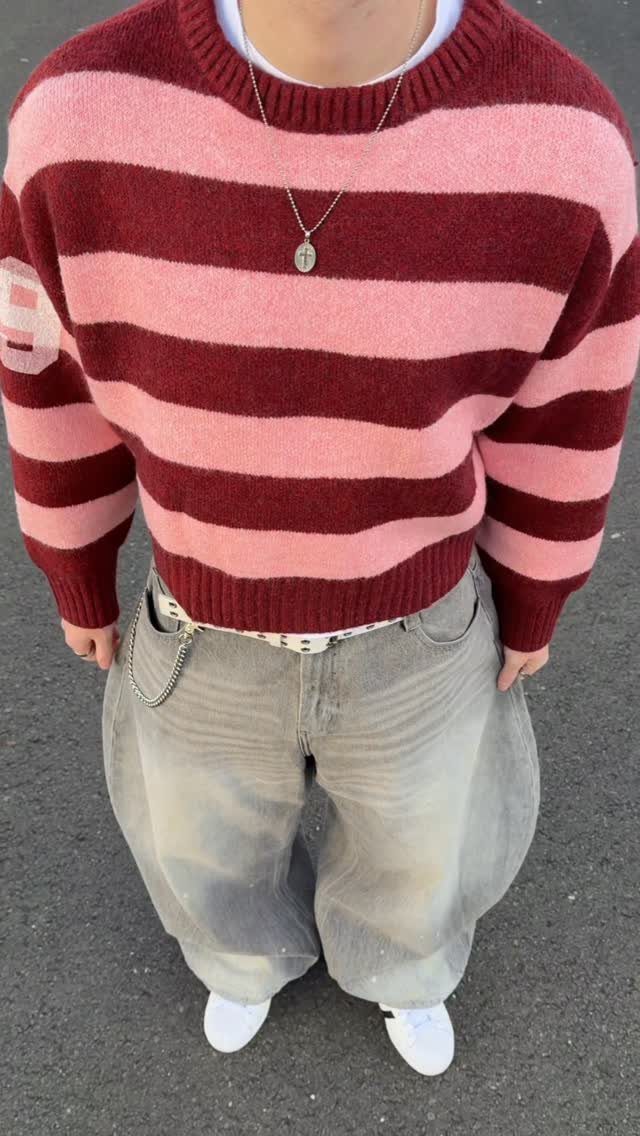 Person wearing a pink and maroon striped cropped sweater with baggy grey jeans and white sneakers.
