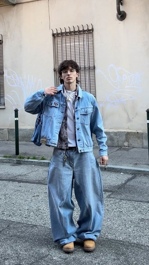 Young man posing in an oversized denim jacket and very wide-leg baggy blue jeans.