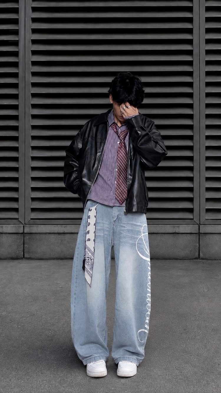 Person wearing light blue baggy jeans with white graphics, a patterned shirt, and a black leather jacket.