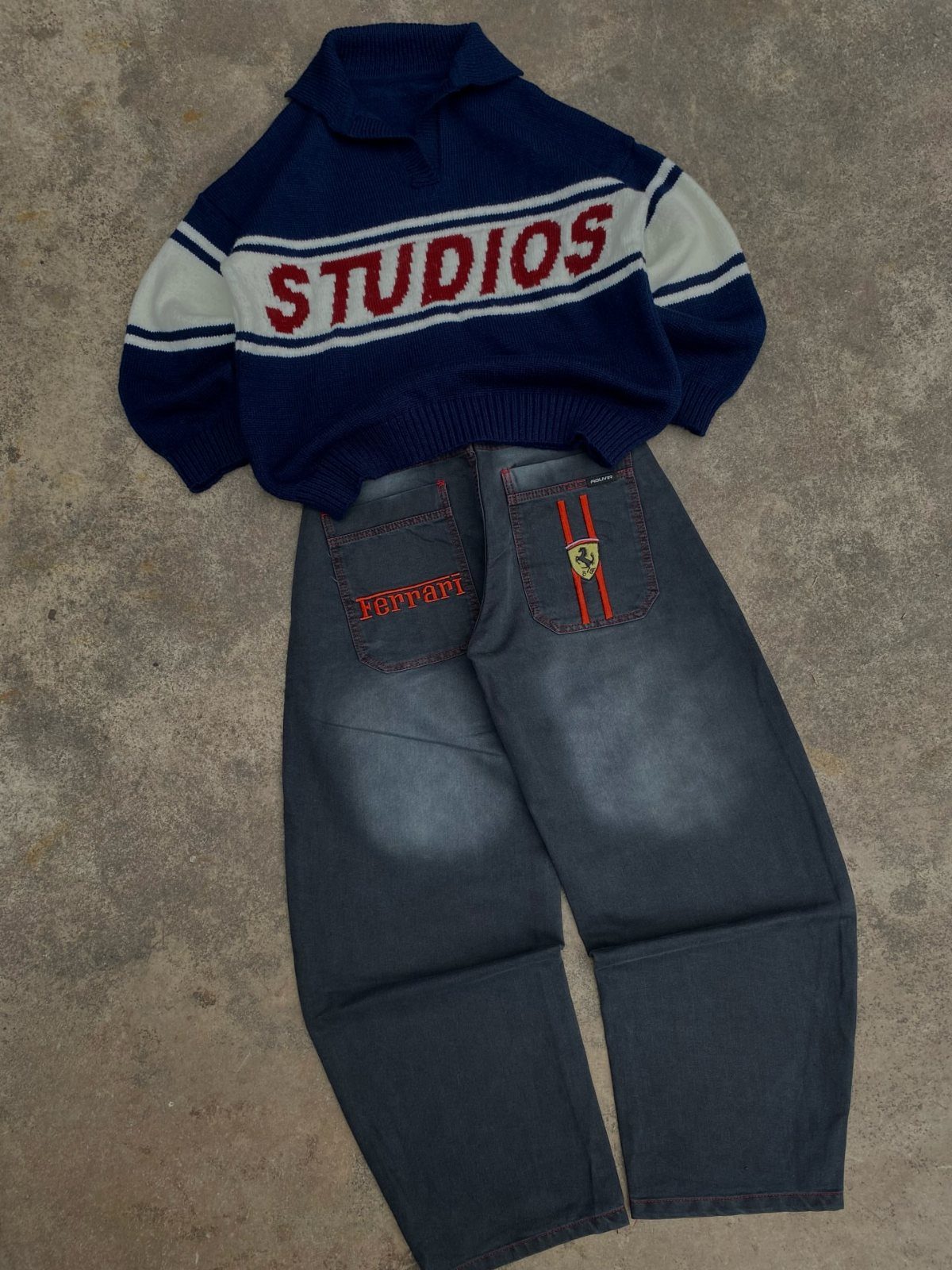 Navy blue oversized sweater with red text and baggy dark denim jeans laid on a grey surface.