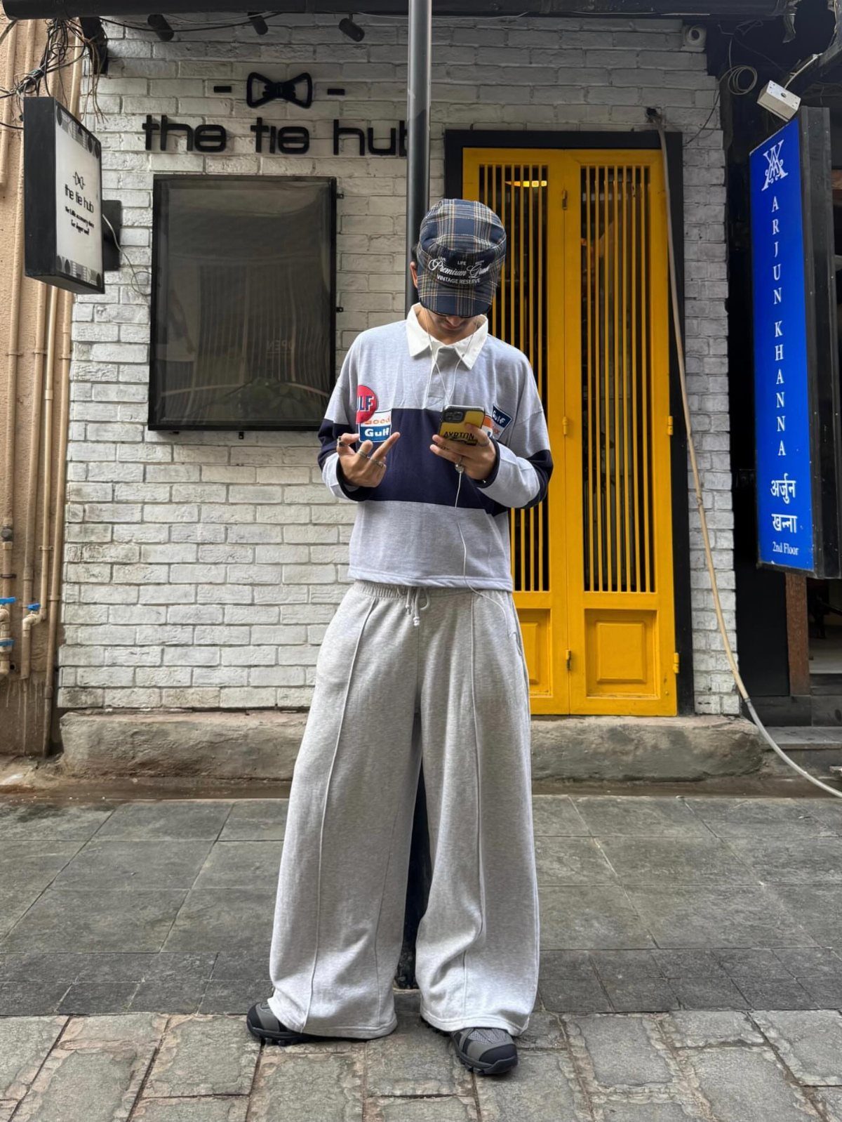 Person wearing oversized grey sweatpants and a long-sleeved polo shirt standing in front of a yellow door.