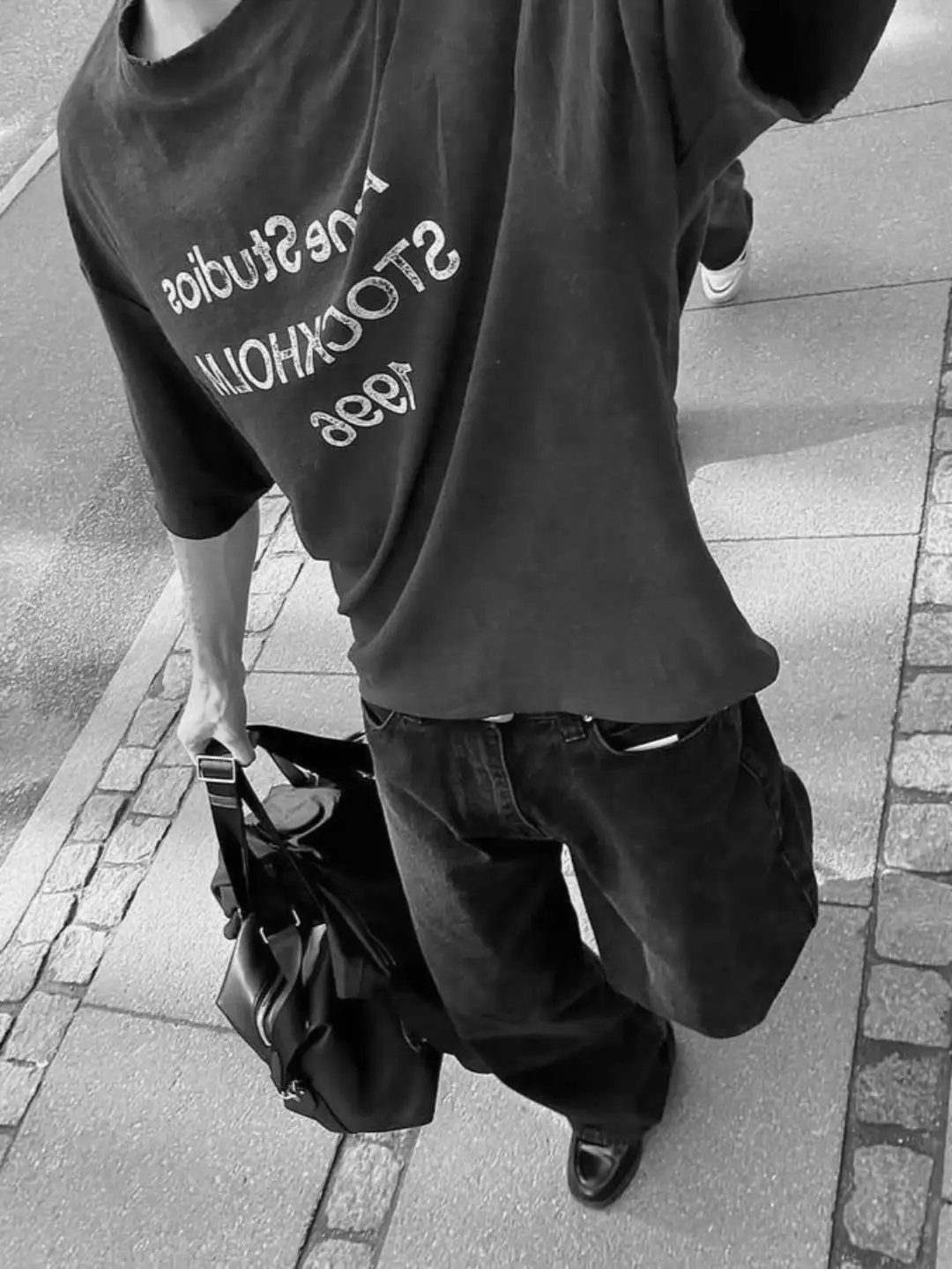 Person wearing an oversized graphic t-shirt and baggy trousers walking on a sidewalk.