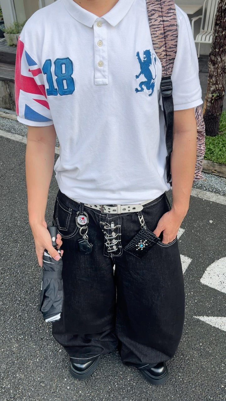 Person wearing a white graphic polo shirt and baggy black denim pants with decorative charms.