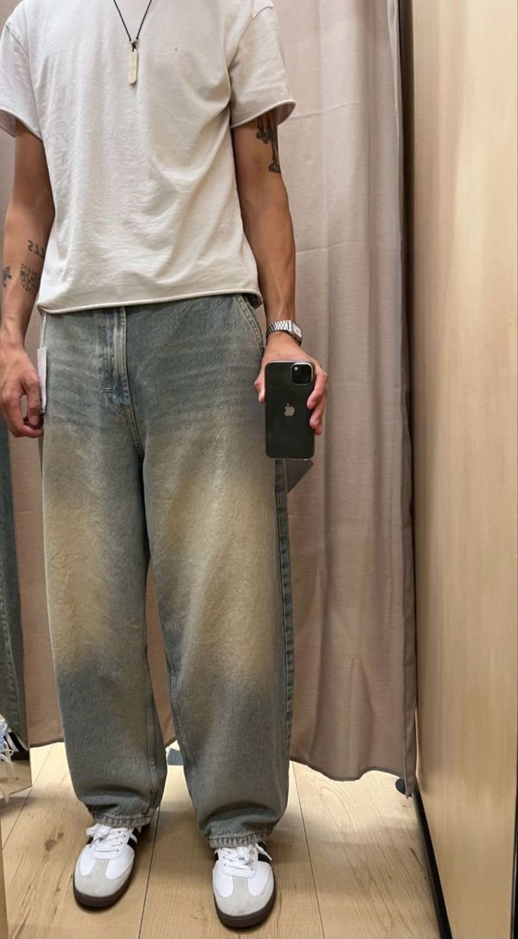 Man wearing an oversized white t-shirt and baggy denim jeans standing in a fitting room.