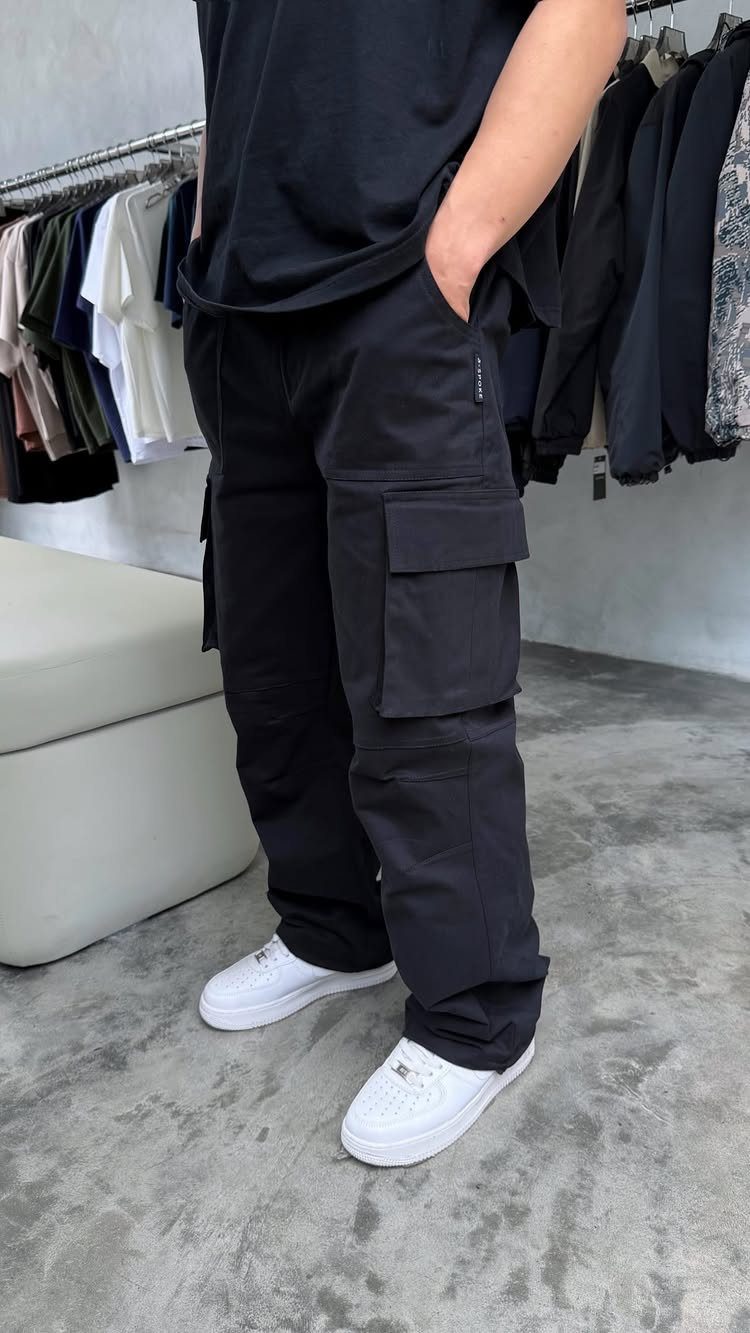 Man wearing black cargo pants, a black t-shirt, and white sneakers in a clothing store.