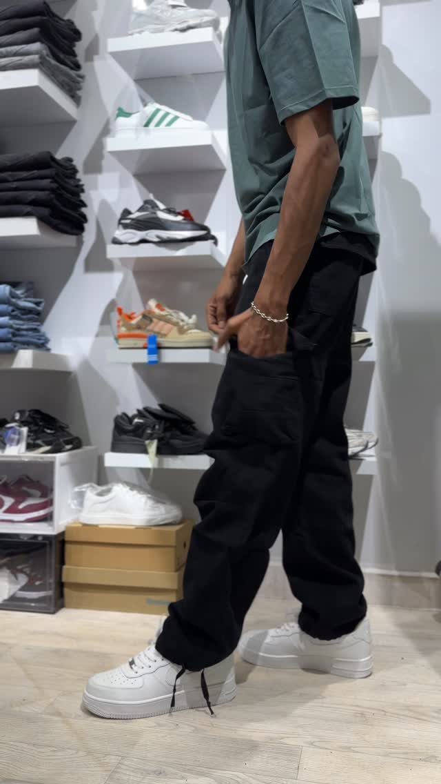 A man wearing black cargo pants, a green t-shirt, and white sneakers in a clothing store.