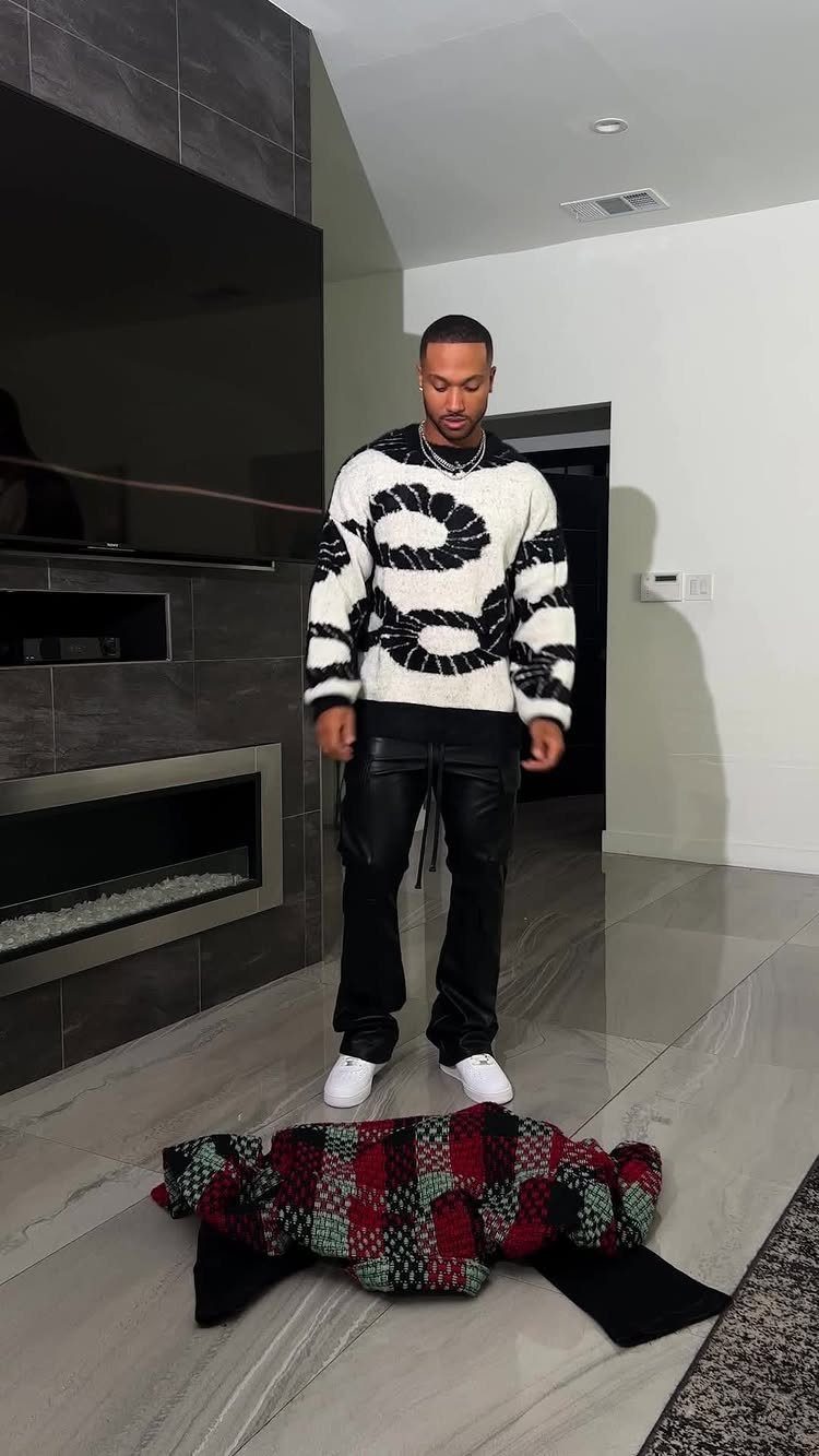 Man wearing a patterned oversized sweater and black leather cargo pants with white sneakers.