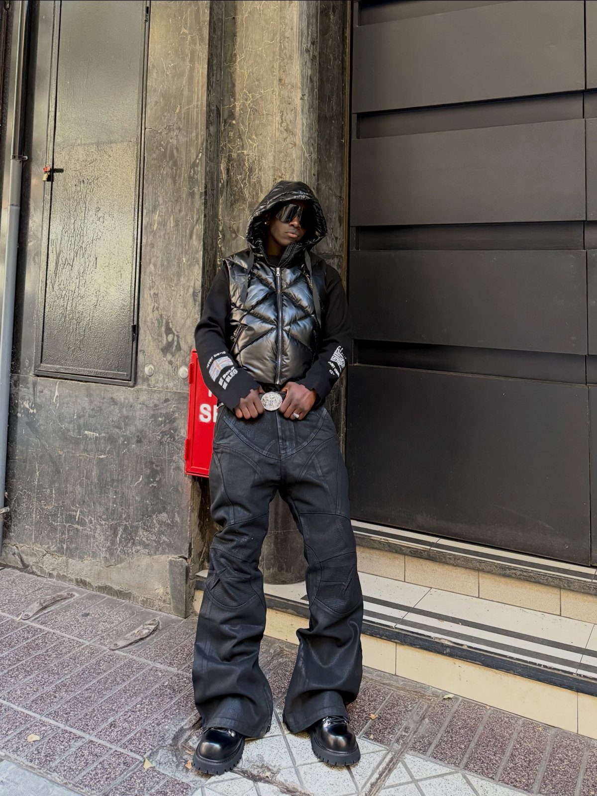 Man wearing a black quilted vest over a black hoodie and wide-leg black cargo pants.