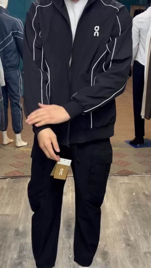 Person wearing a black athletic jacket with white lines and black cargo pants.