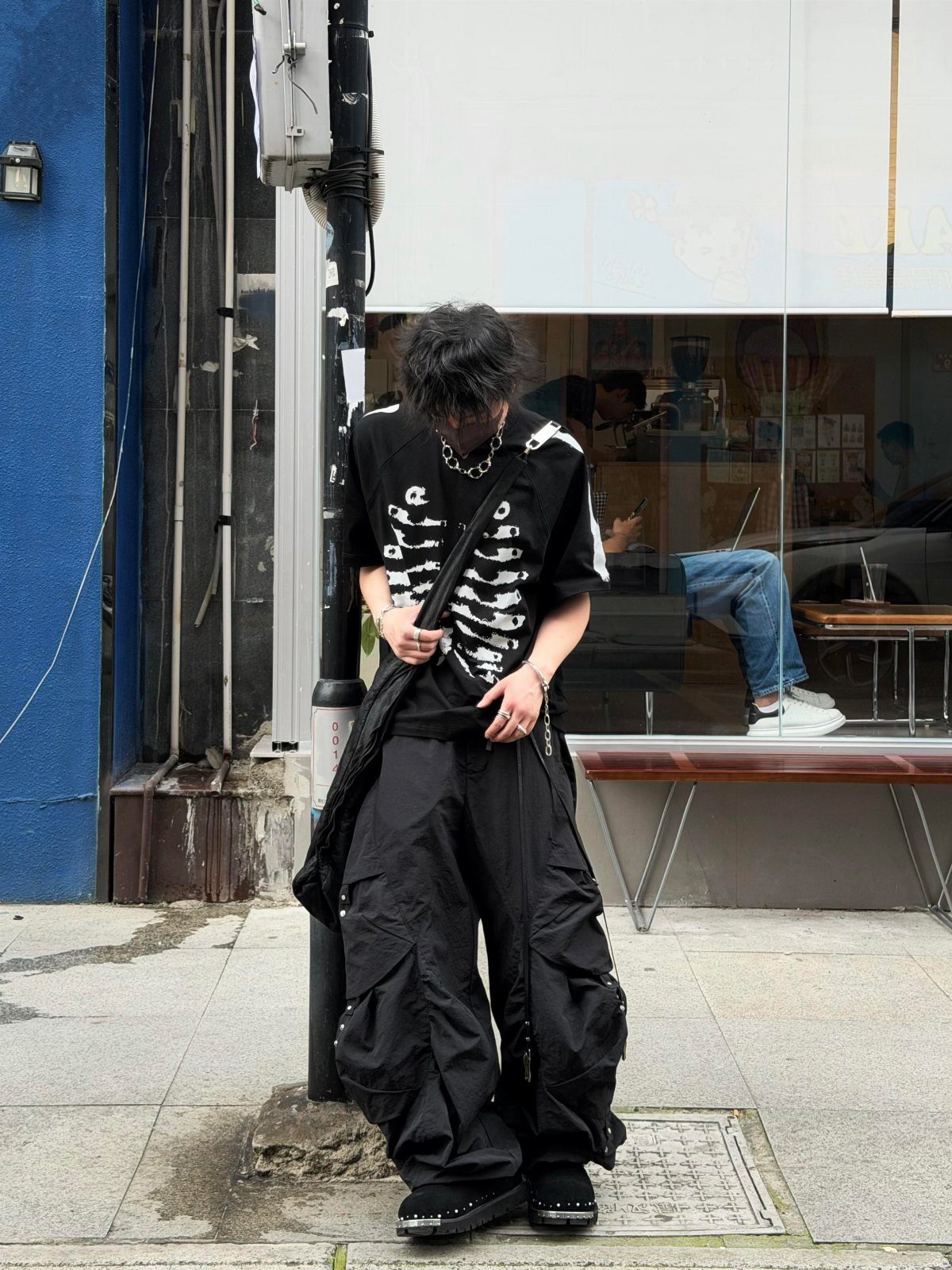 Person wearing a black skeleton graphic t-shirt and baggy black cargo pants standing on a sidewalk.