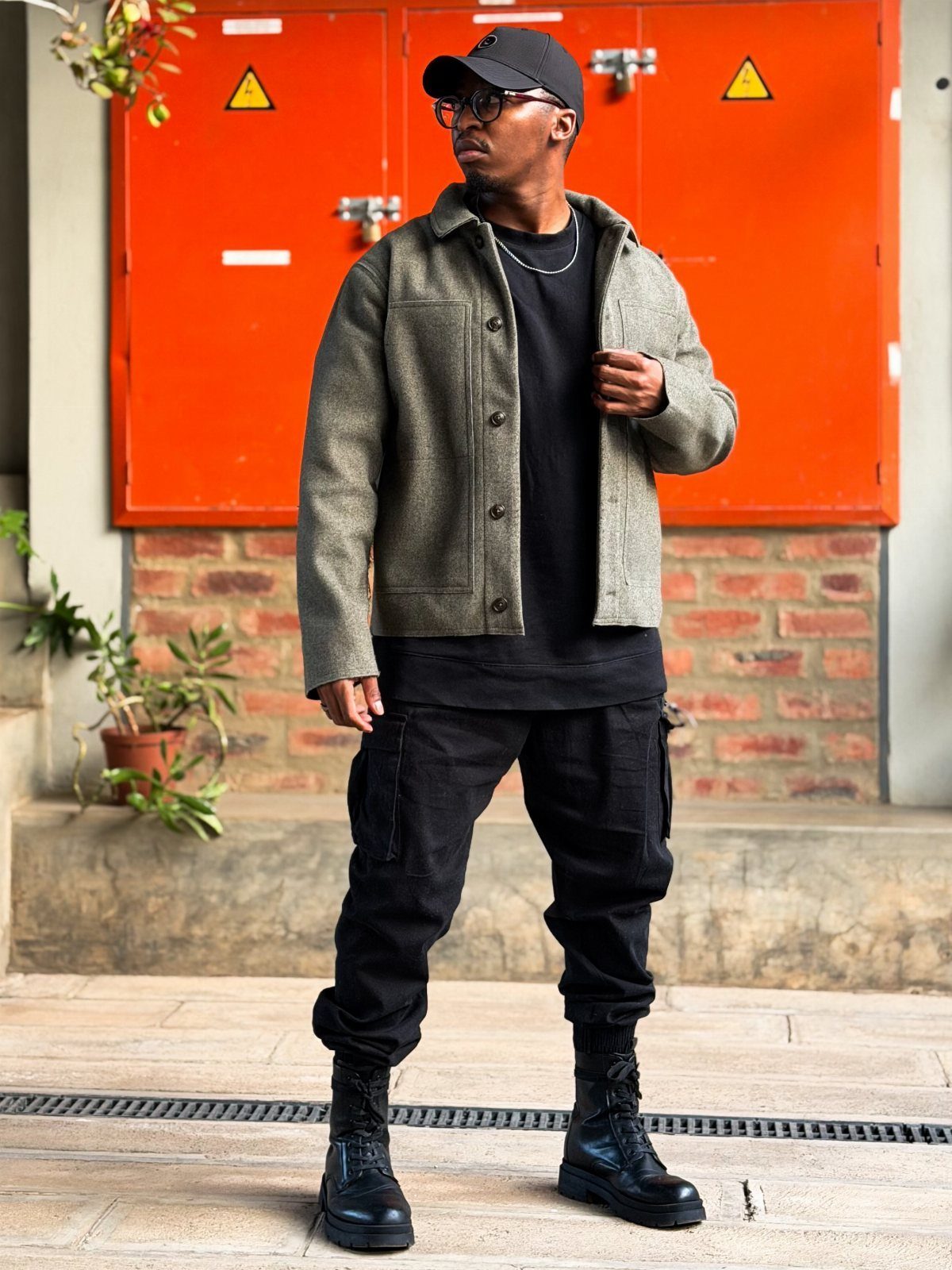 Man wearing a grey textured jacket, black t-shirt, black cargo pants, and combat boots.