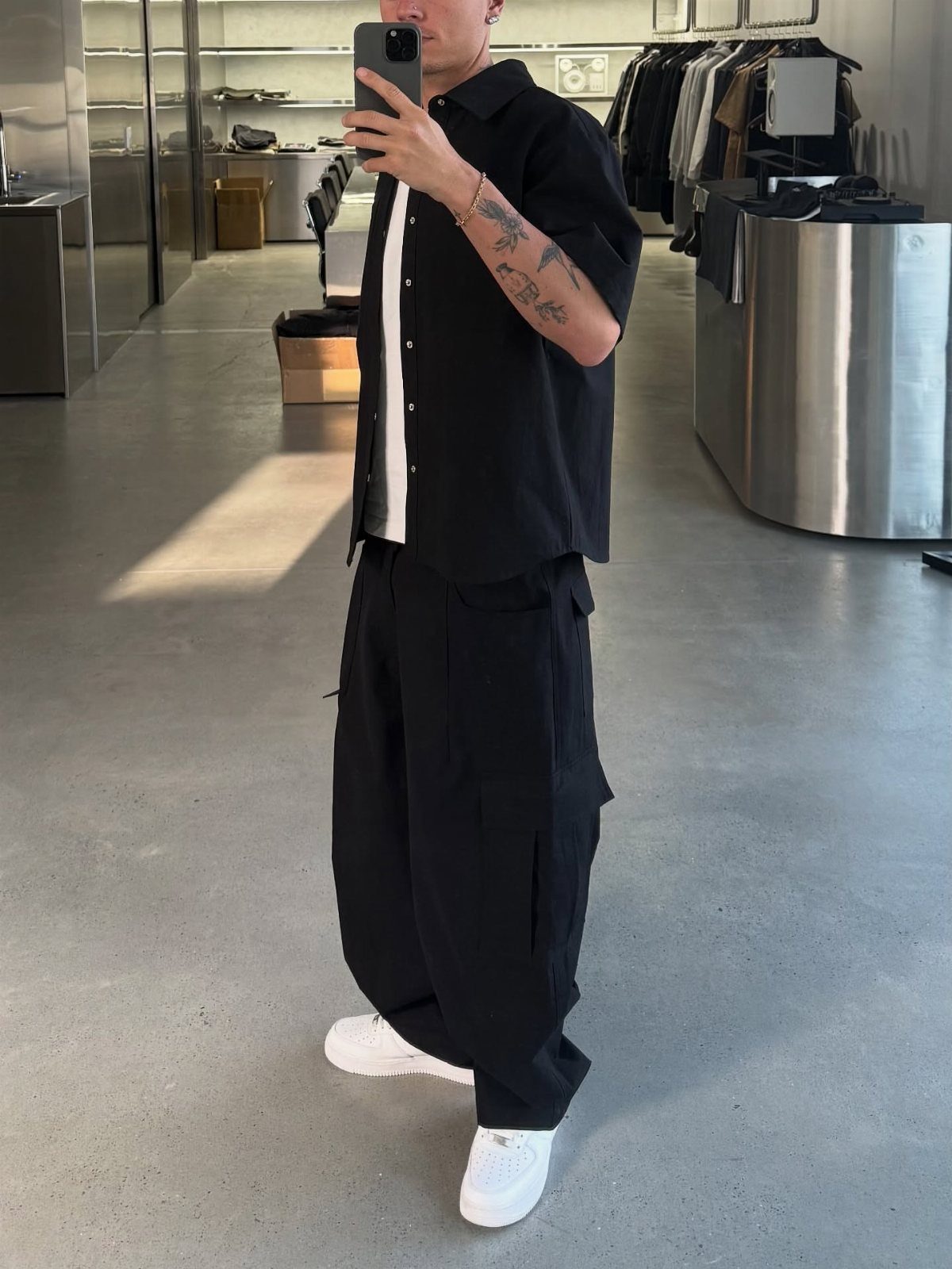Person in black cargo pants, black shirt, and white sneakers taking a mirror selfie.
