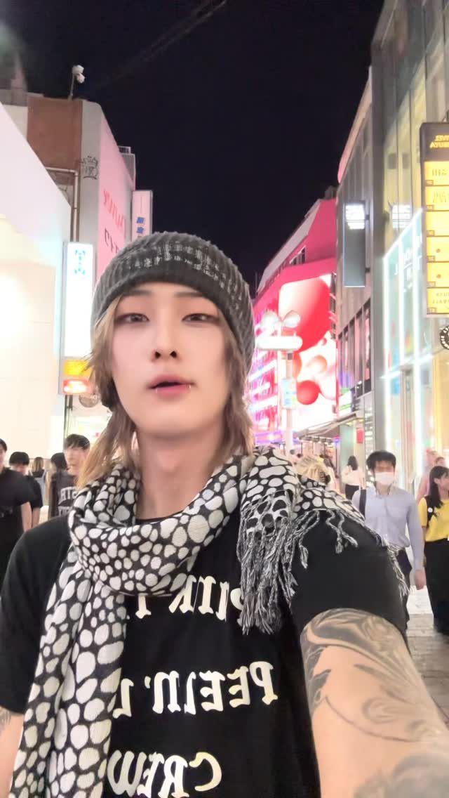 A young man wearing a dark grey knit beanie and a patterned scarf on a city street.