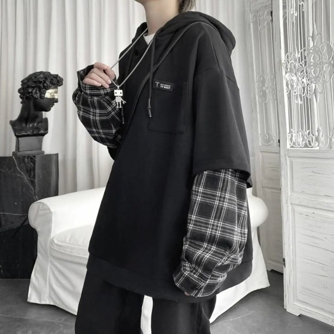 Person wearing an oversized black hoodie with grey plaid patterned sleeves.