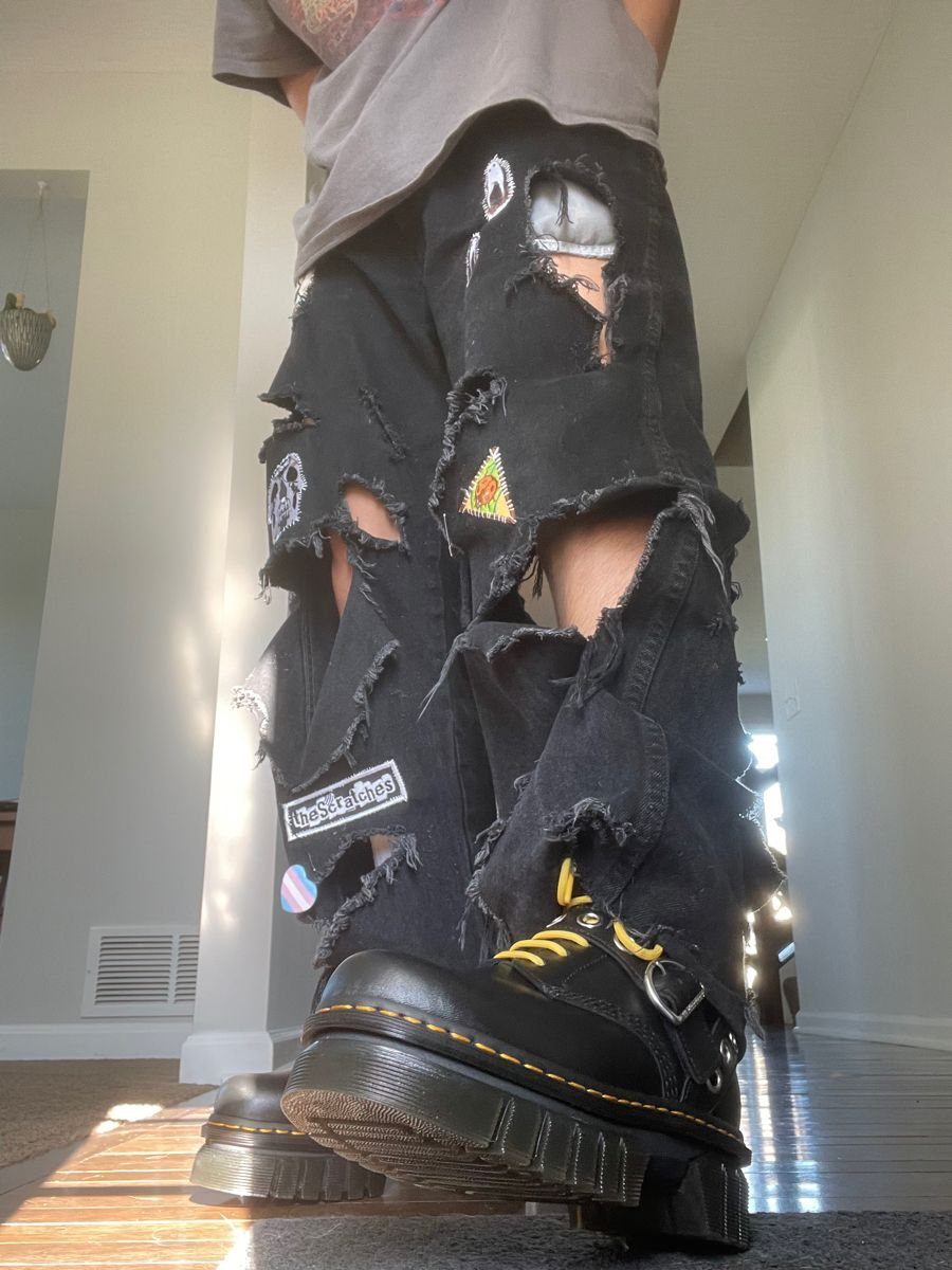 Distressed black ripped denim pants paired with black combat boots with yellow laces.