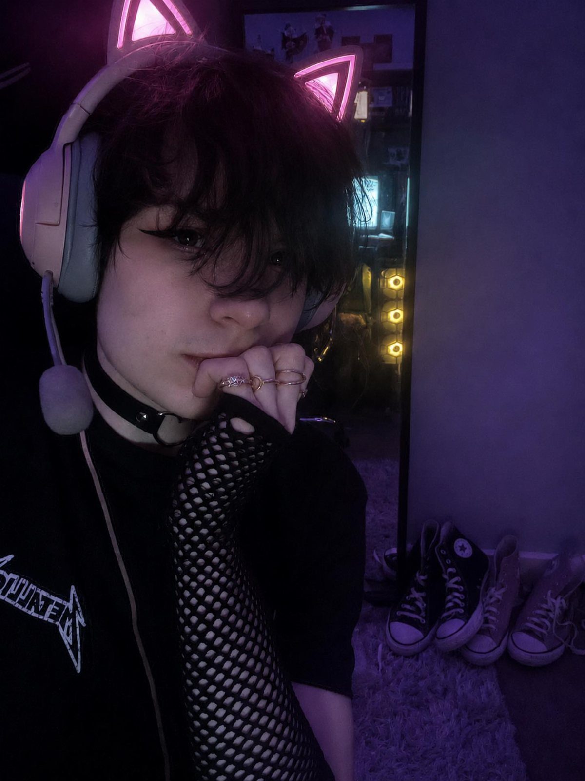 Person wearing black fishnet sleeves, a choker, and cat-ear headphones in dim lighting.