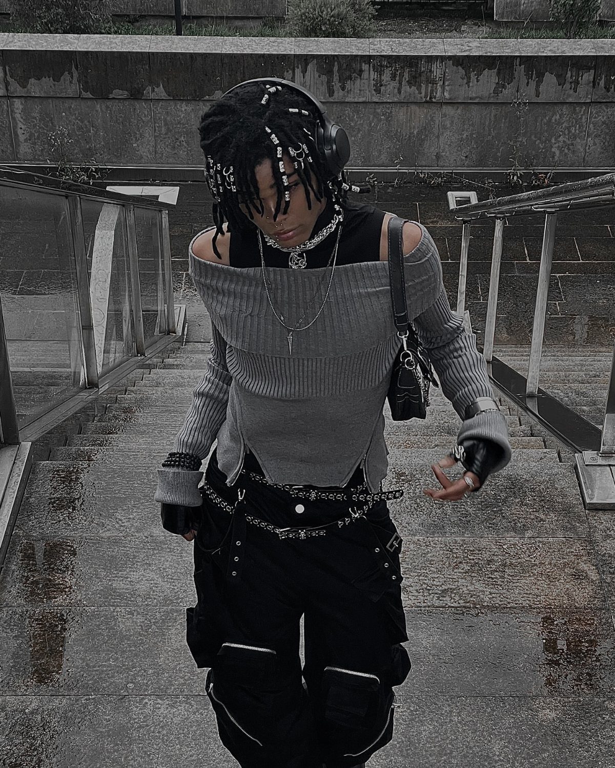 A person in alternative fashion walking down concrete stairs wearing silver chains and a grey ribbed top.