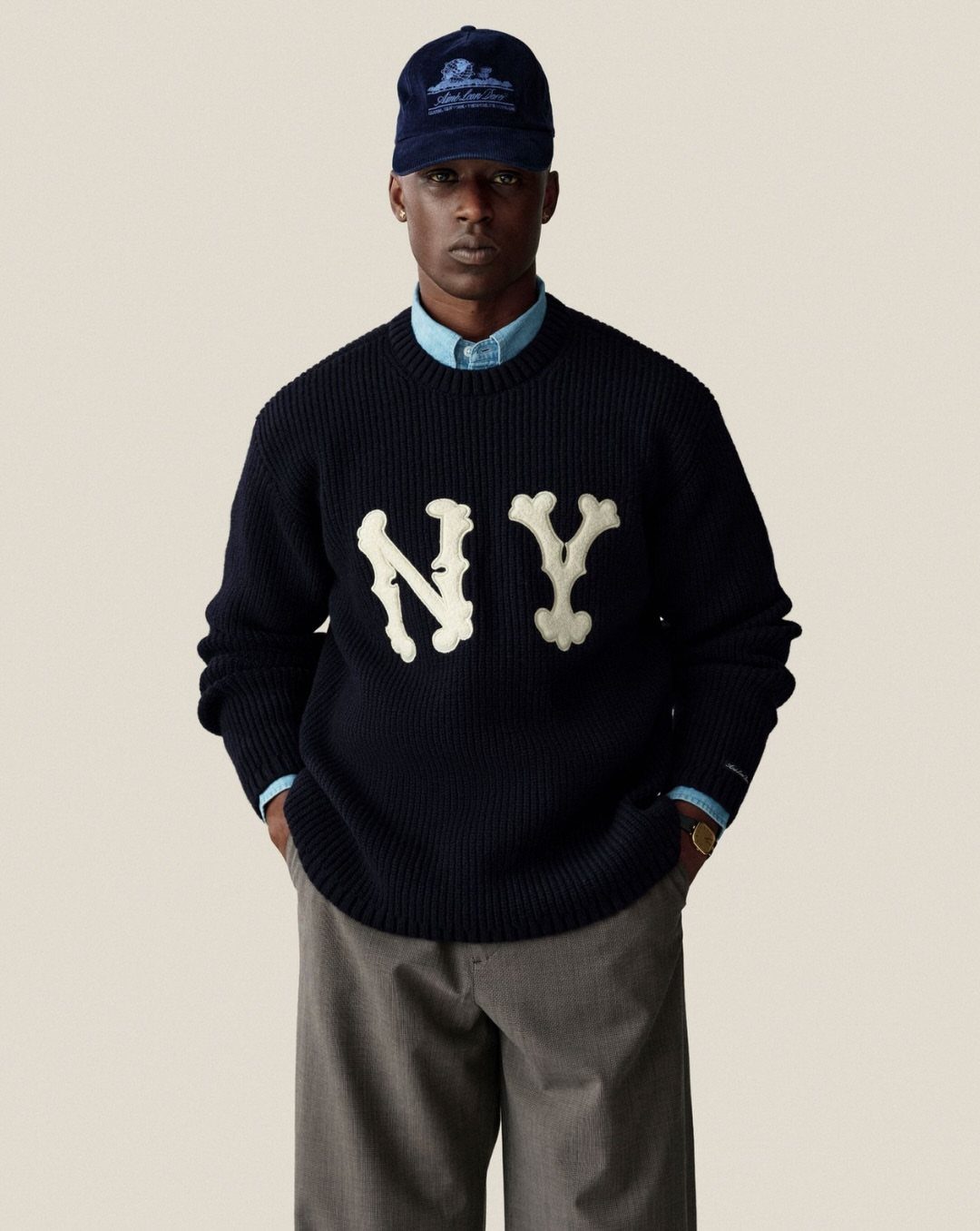 Man wearing a navy ribbed sweater with white NY lettering and a blue baseball cap.