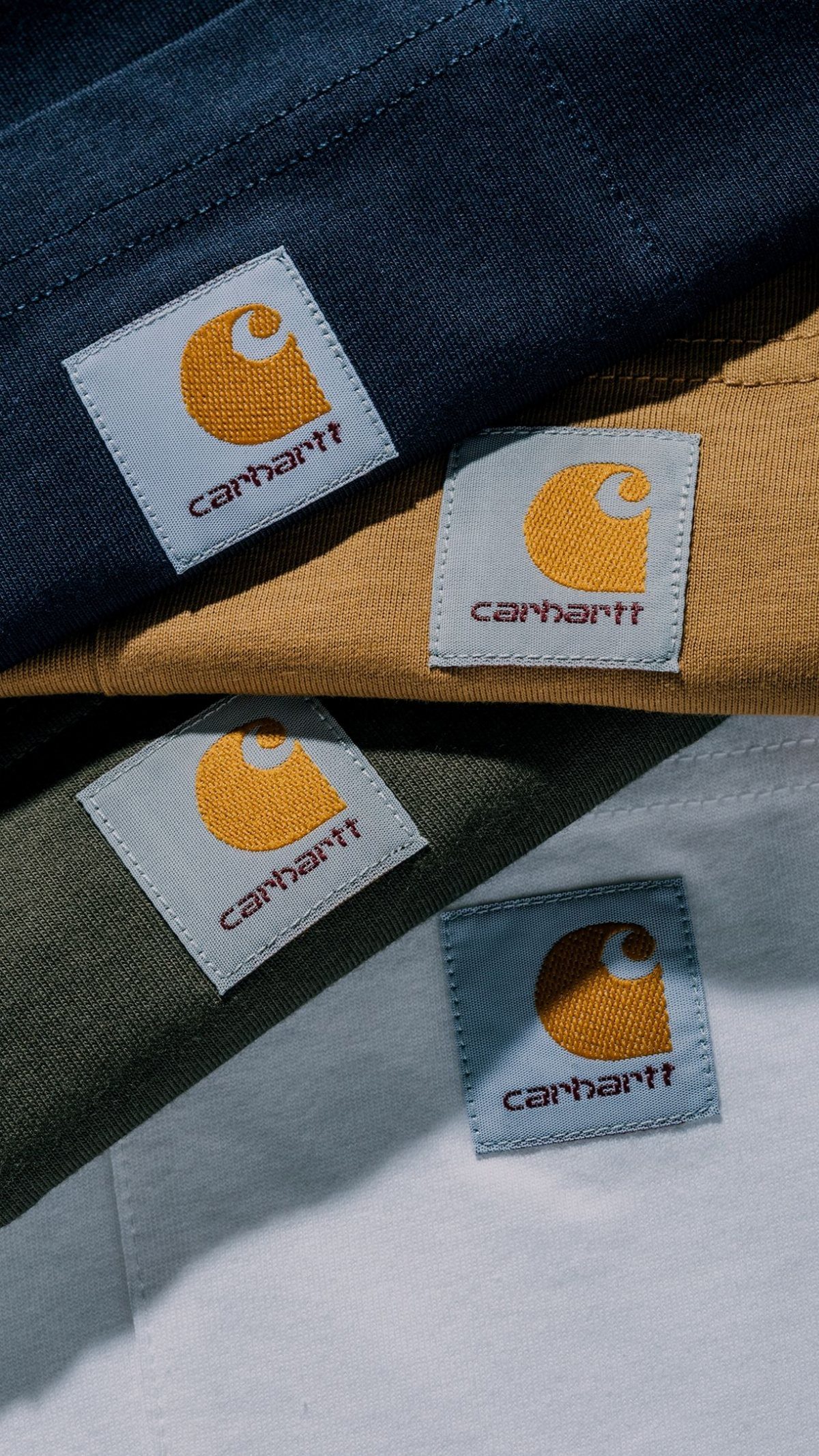 Four Carhartt brand patches sewn onto navy, yellow, green, and white fabric pieces.