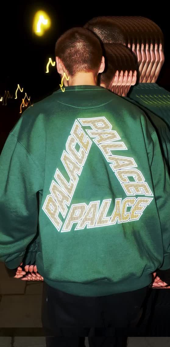 Person wearing a green Palace Skateboards sweatshirt with a large triangular logo on the back.