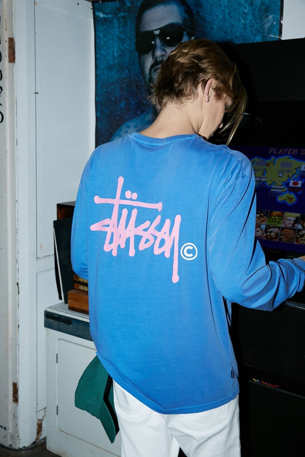 Person wearing a blue long-sleeve shirt with a large pink Stüssy logo on the back.