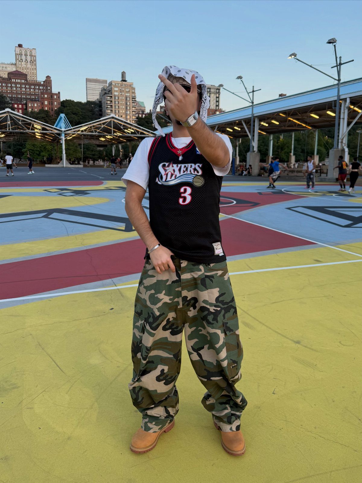 Person wearing a black basketball jersey and camouflage cargo pants on a colorful outdoor basketball court.