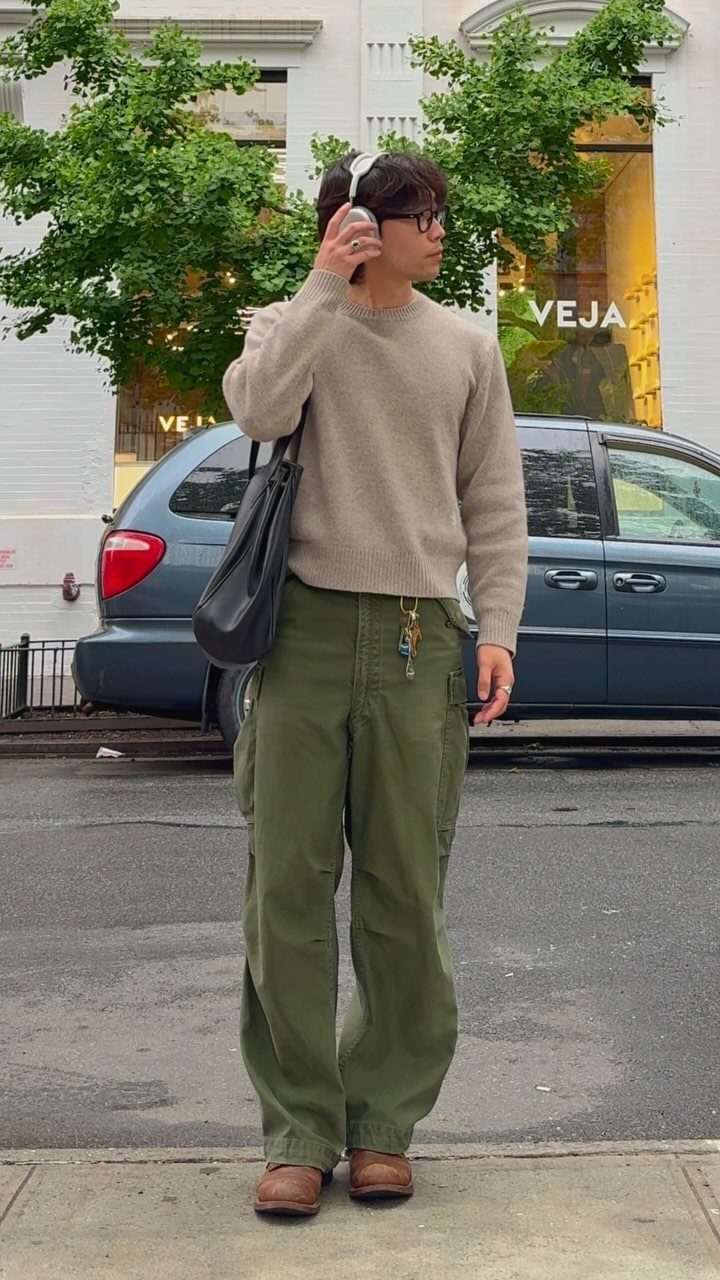 Person wearing olive green baggy cargo pants and a beige sweater standing on a city street.