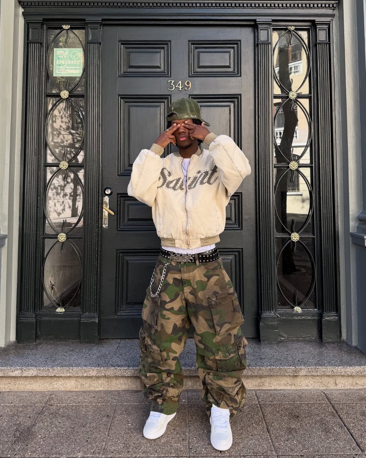 A person posing in camouflage cargo pants, a cream bomber jacket, and white sneakers.