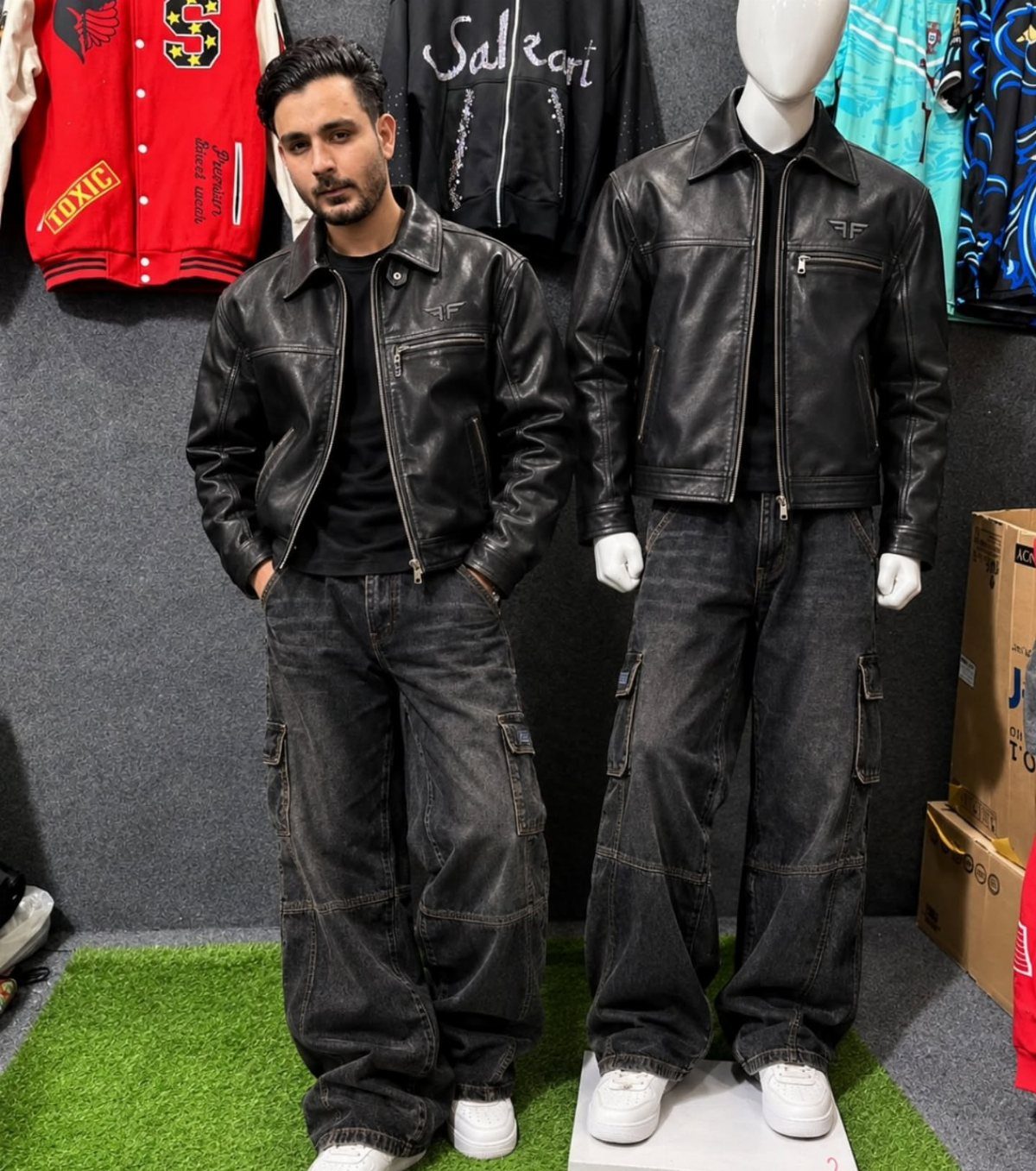 Man and mannequin wearing black leather jackets and baggy black cargo pants in a shop.