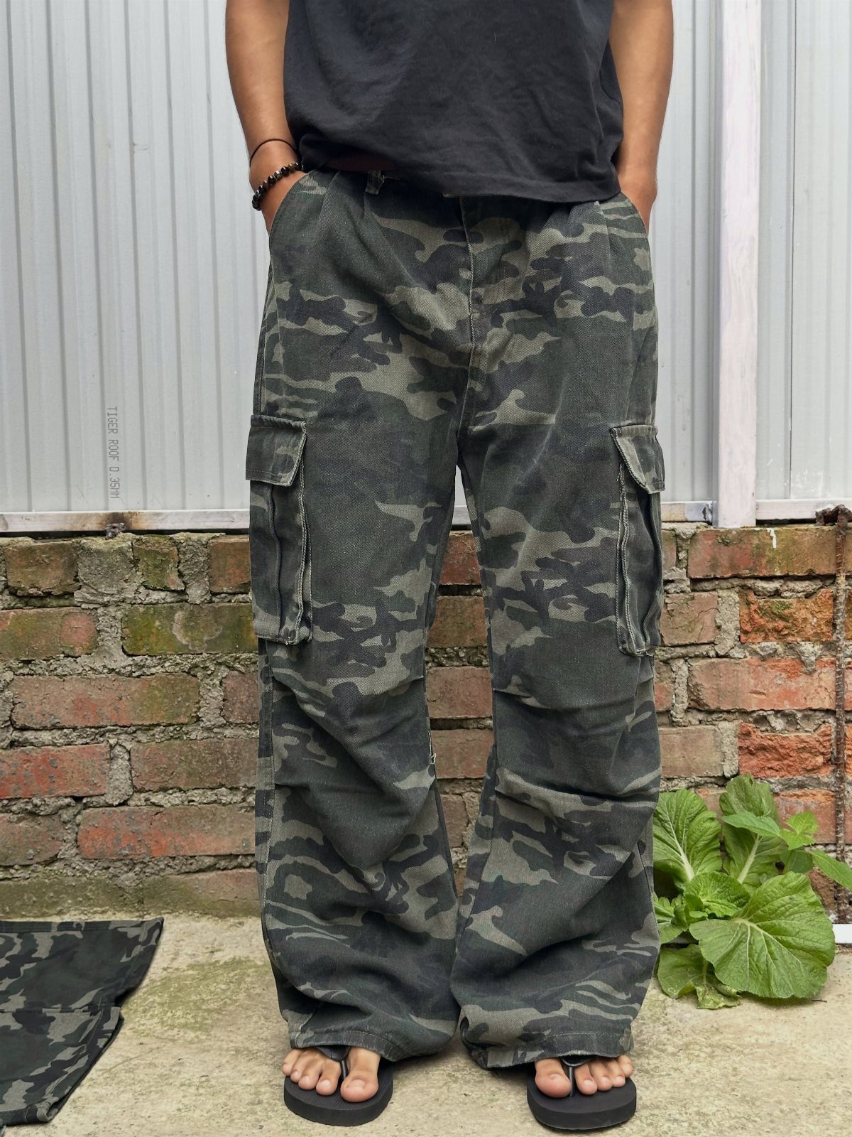 Person wearing baggy camouflage cargo pants and a black t-shirt standing outdoors.