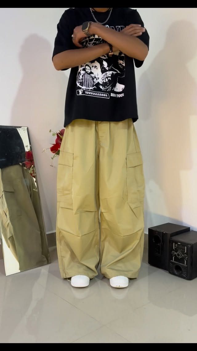 A person wearing oversized khaki cargo pants and a black graphic t-shirt standing indoors.