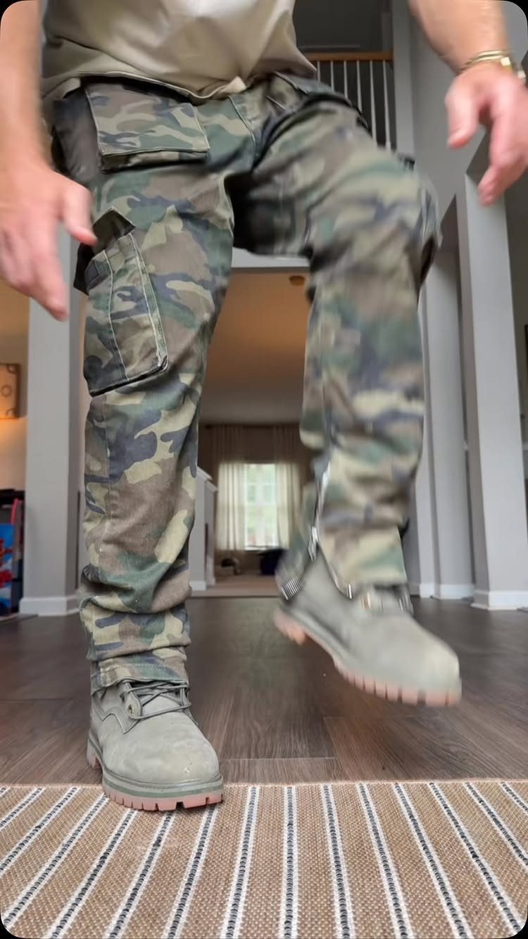 Person wearing camouflage cargo pants and grey boots walking on a striped rug.
