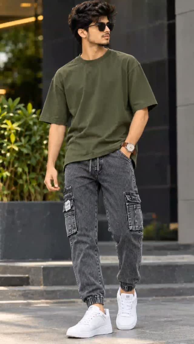 Man in olive t-shirt and grey cargo pants posing outdoors wearing white sneakers.