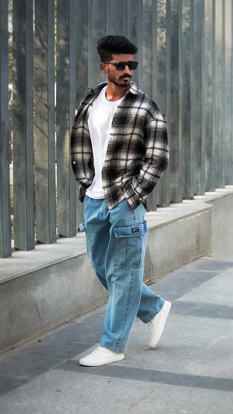 A man walking in light blue denim baggy cargo pants, a plaid shirt, and white sneakers.