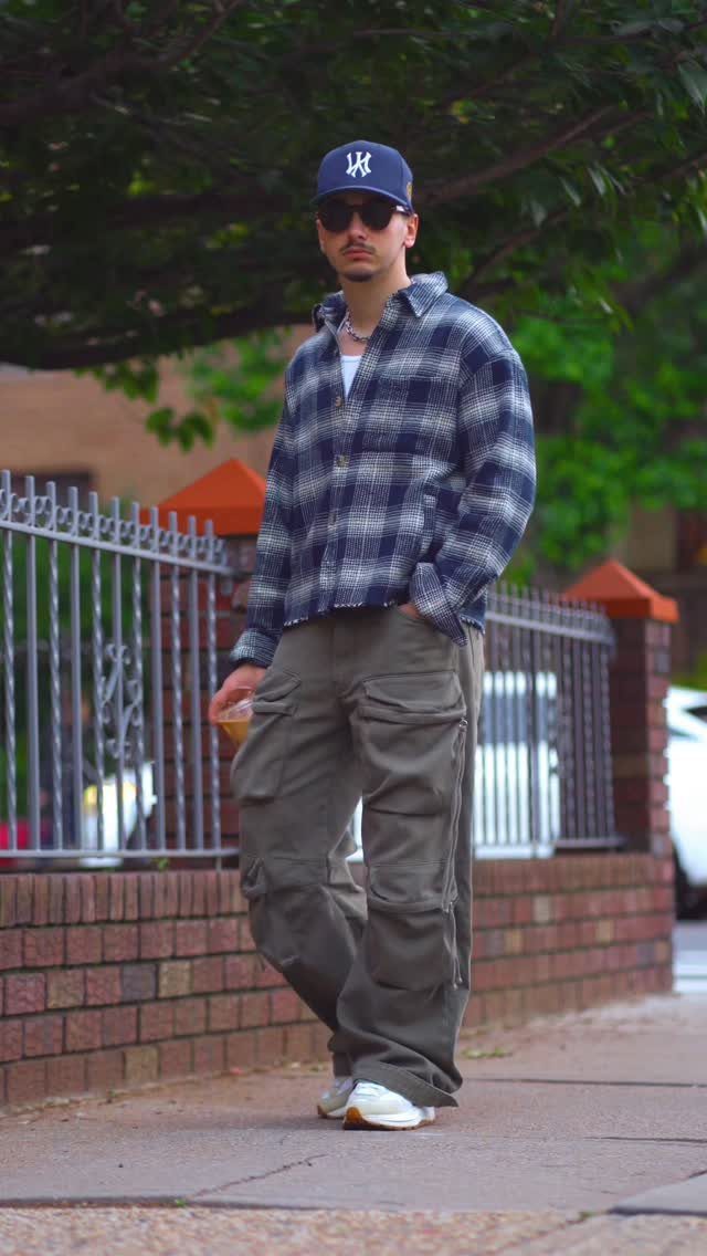Man walking outdoors wearing olive green cargo pants and a blue plaid flannel shirt.