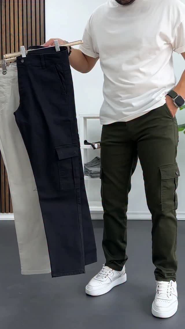 A man wearing olive green cargo pants and white sneakers standing next to a clothing rack.