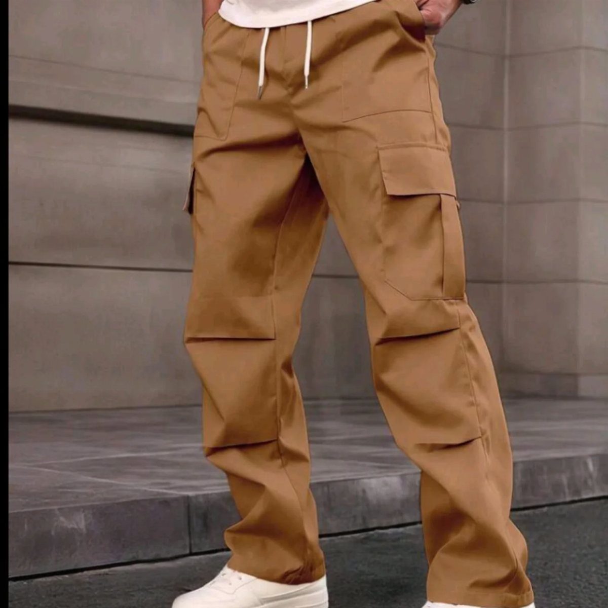 A person wearing tan cargo pants with large pockets and white sneakers against a stone wall.