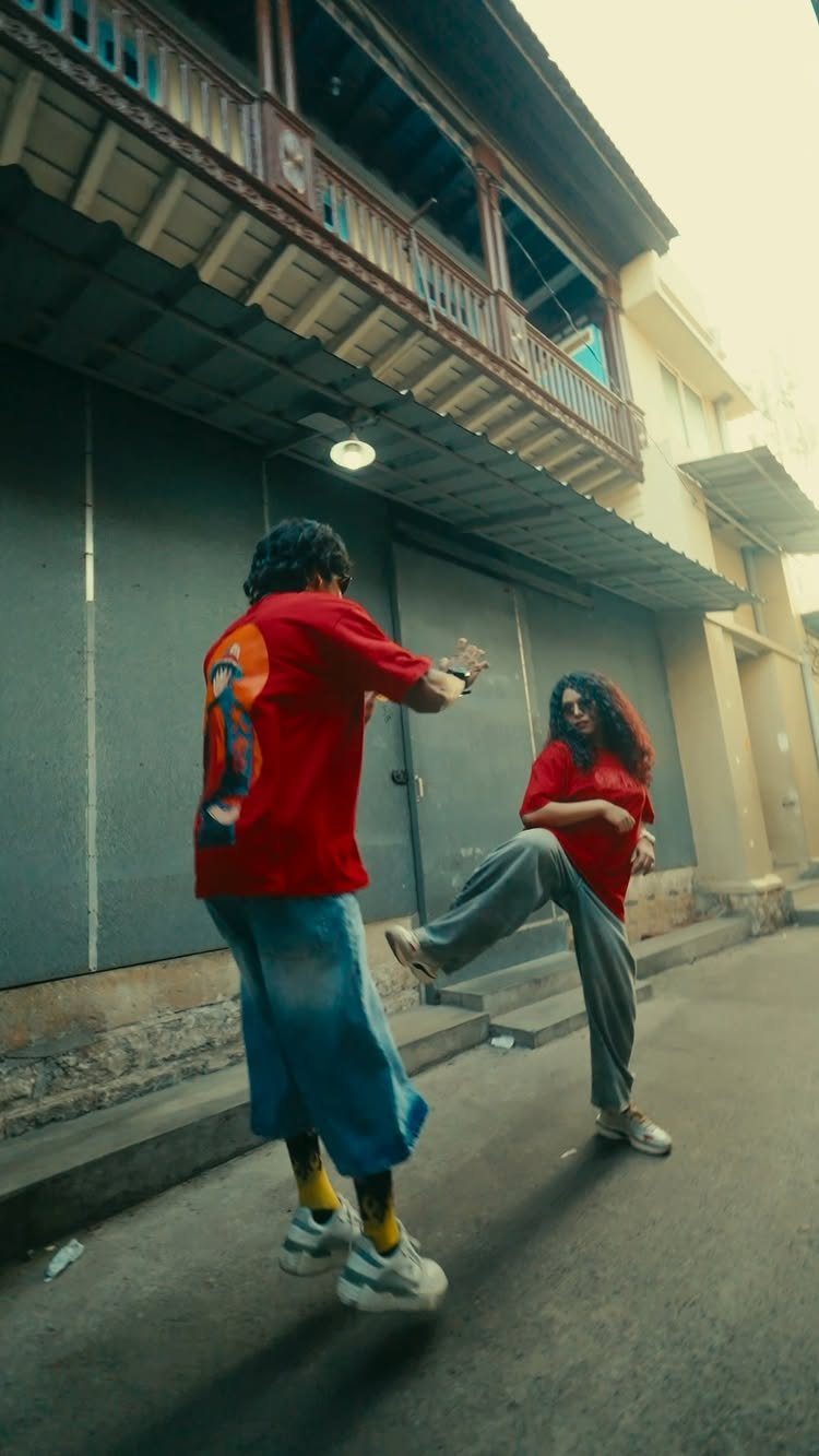 Two people wearing red graphic t-shirts and casual pants while posing on a city street.