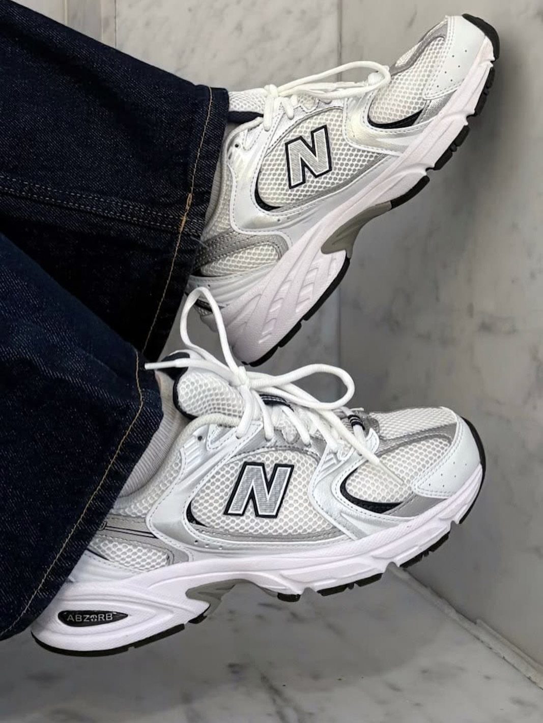 White New Balance sneakers with grey accents worn with dark blue denim jeans.