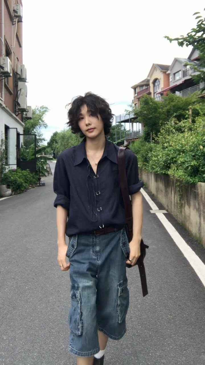 A person wearing a navy shirt and oversized denim cargo shorts standing on a street.