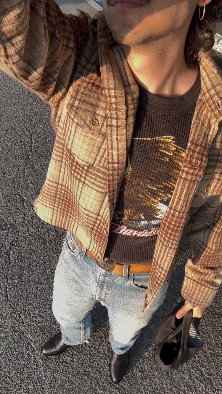 Person wearing light blue jeans, a plaid shirt, and black cowboy boots standing on asphalt.