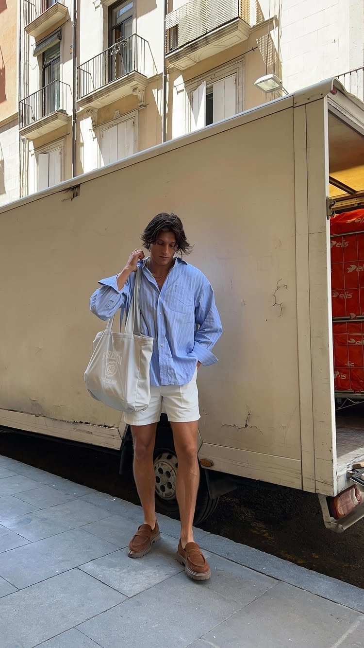 A young man in a blue striped shirt and white shorts stands by a white truck.
