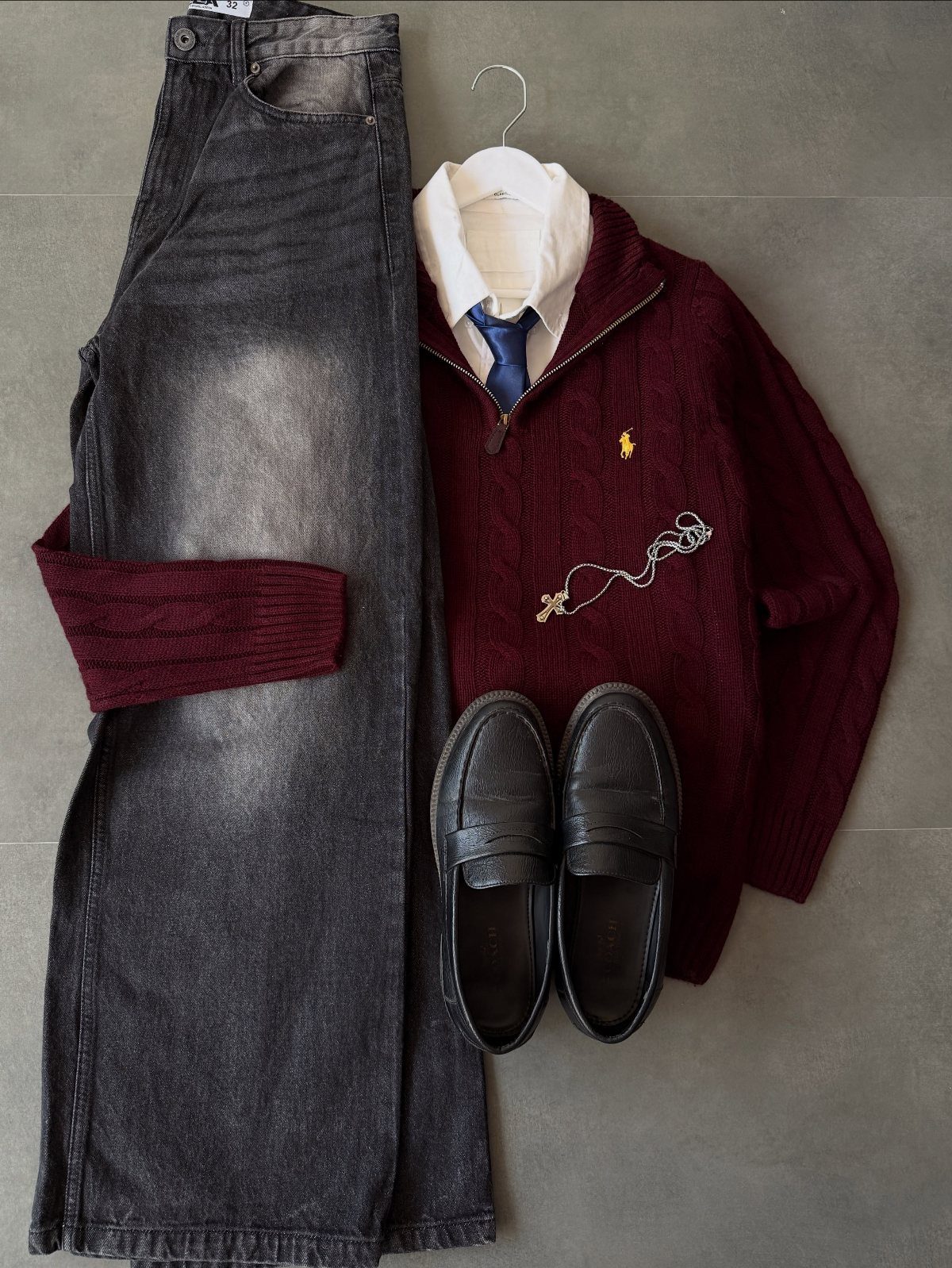 Burgundy cable knit sweater, white shirt, blue tie, grey trousers, and black loafers laid out.