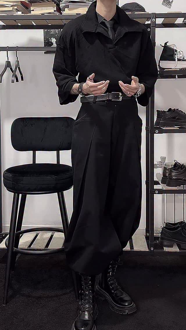 A person dressed in an all-black dark academia style outfit with wide trousers and combat boots.
